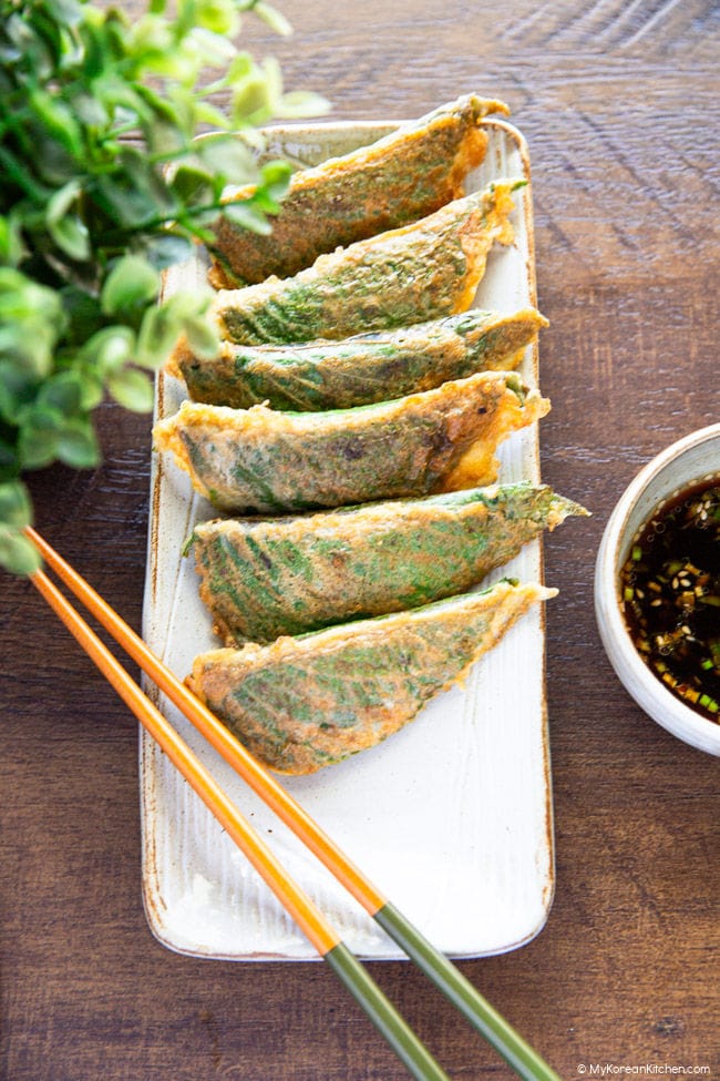 Pan-fried stuffed perilla leaves on a slim rectangular plate with chopsticks on the left and dipping sauce on the right