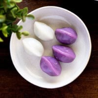 Purple and white songpyeon served on a small white plate on a wooden board