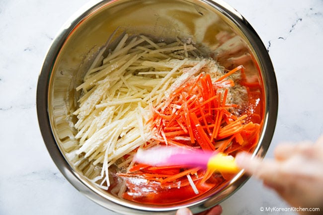 Mixing potato and carrot pancake batter in a bowl.