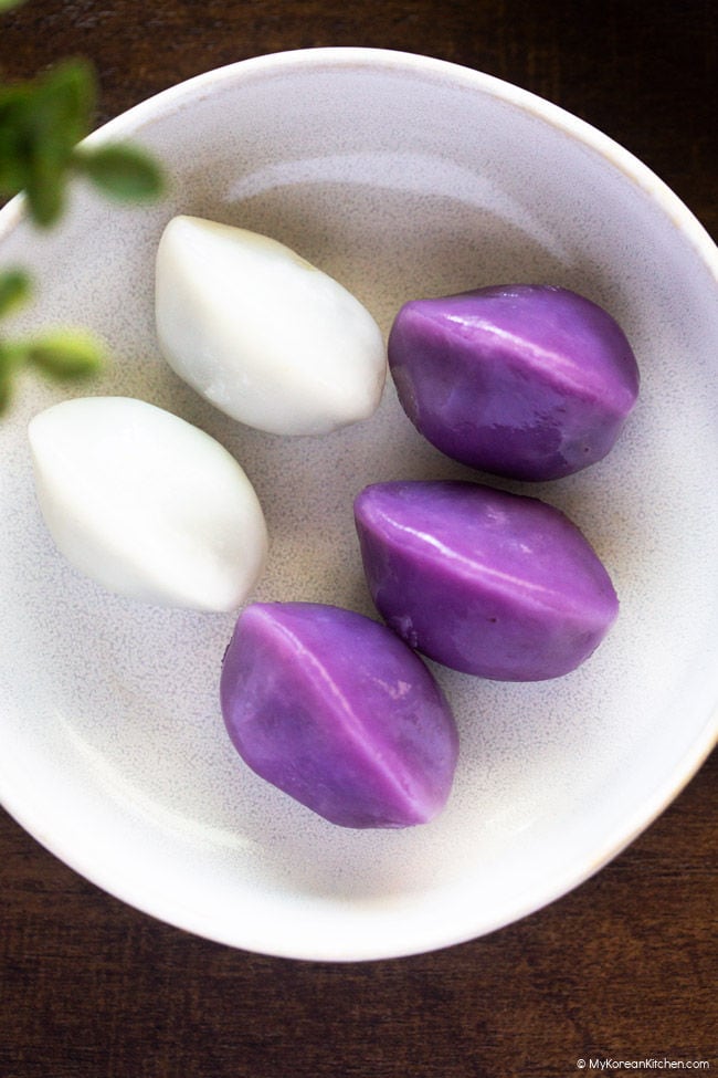Close-up of three purple and two white songpyeon served on a small plate