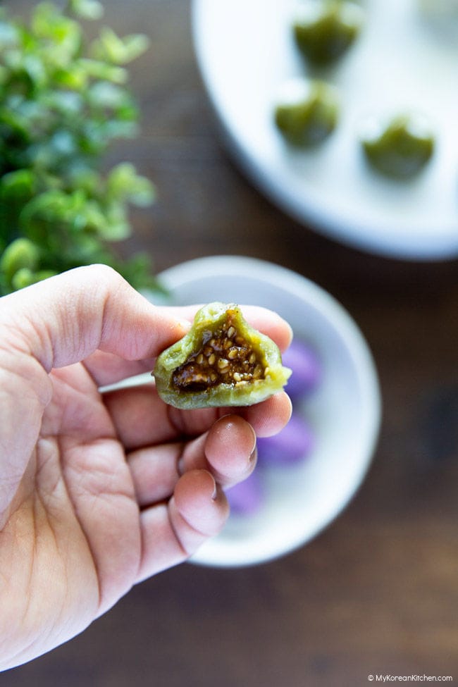 Holding a half-bitten songpyeon to show the honey sesame filling inside.