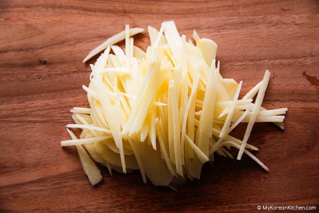 Julienned potatoes for gamja-chae jeon placed on a wooden cutting board.