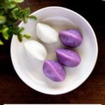 Purple and white songpyeon served on a small white plate on a wooden board