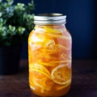 Glass jar of Korean lemon ginger syrup filled with thin lemon slices and honey, set against a dark navy background with soft natural light.