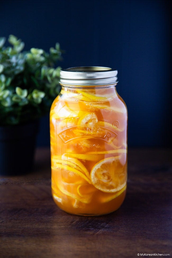 Glass jar of Korean lemon ginger syrup filled with thin lemon slices and honey, set against a dark navy background with soft natural light.