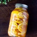 Angled view of a glass jar filled with Korean lemon ginger syrup, showing vibrant lemon slices in golden honey syrup on a rustic wooden background.