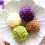 Hand holding a small flower-shaped plate with four colorful sweet rice balls.