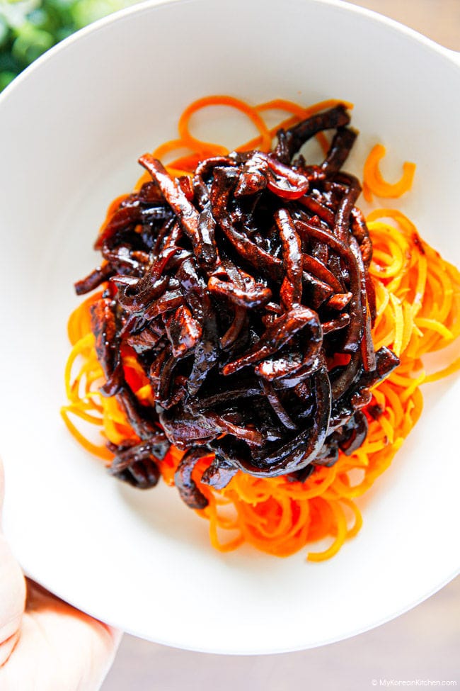 Holding a bowl of carrot noodles topped with black bean sauce