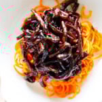 Holding a bowl of carrot noodles topped with black bean sauce
