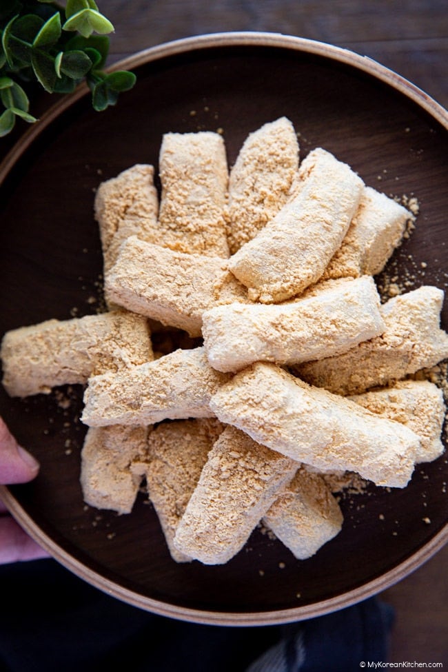 Close-up of hands holding a small wooden plate with injeolmi Korean rice cake