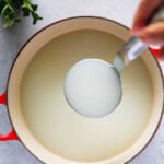 Holding milky Korean beef bone broth in a ladle over a pot of cooked beef bones