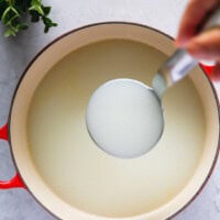 Holding milky Korean beef bone broth in a ladle over a pot of cooked beef bones