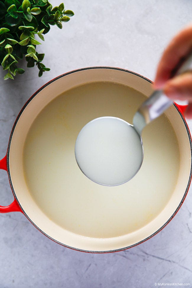Holding milky Korean beef bone broth in a ladle over a pot of cooked beef bones