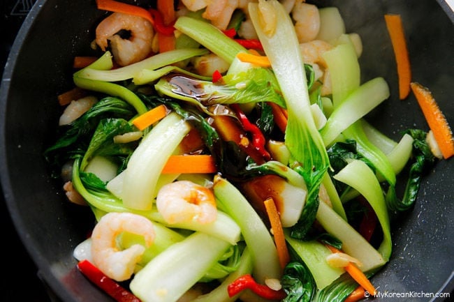 adding sauce to sautéed vegetables in a wok