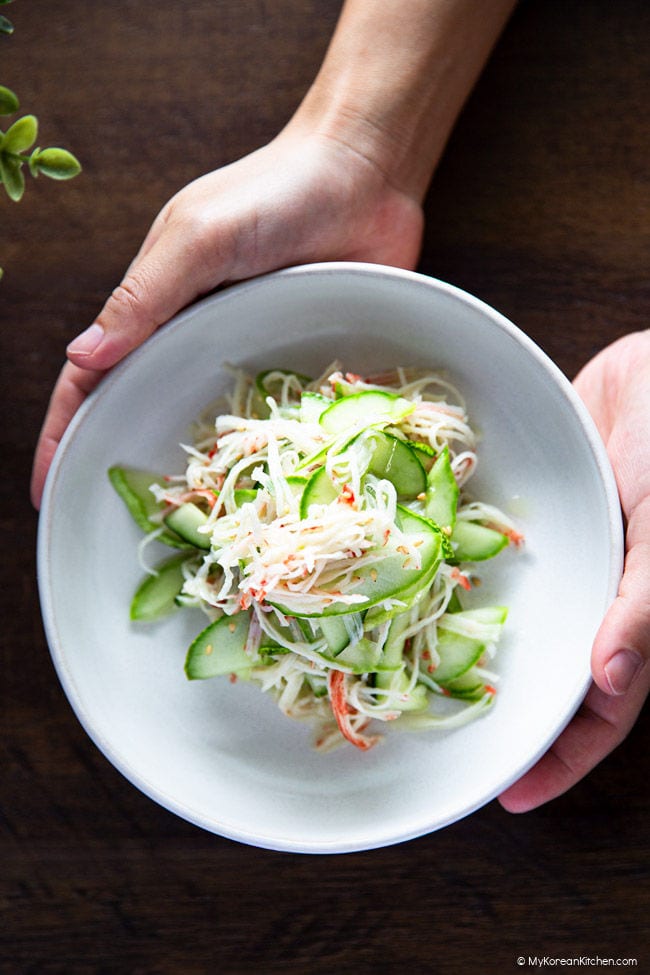 holding a plate of Korean cucumber crab salad with both hands