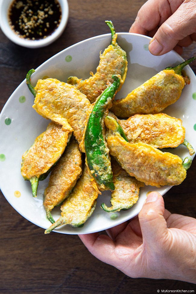 Holding a plate filled with golden Korean stuffed chili peppers with both hands.