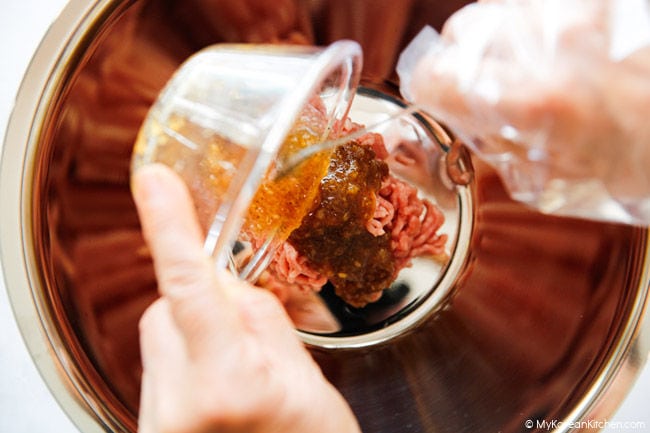 Pouring the seasoning sauce over pork mince in a stainless steel mixing bowl.