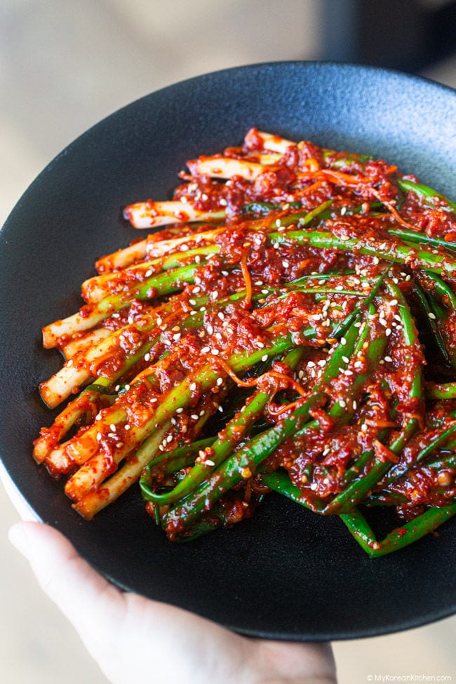 hands holding a shallow black bowl of pa kimchi