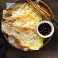 Baechujeon served on a wooden plate with chopsticks and a bowl of dipping sauce.