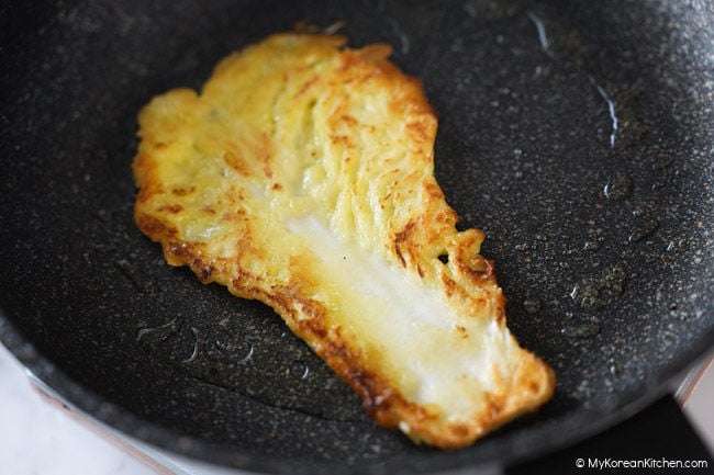 Baechujeon being turned over in a frying pan.