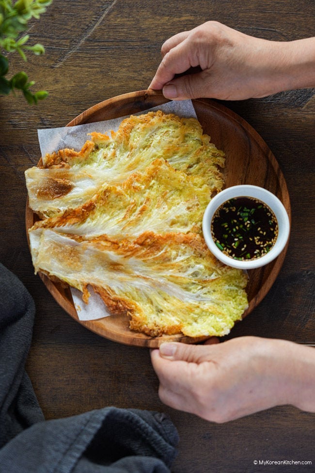 Holding a wooden plate of Korean cabbage pancakes.