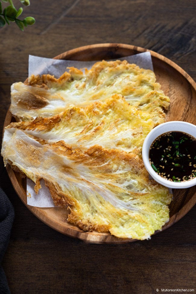 Korean cabbage pancakes served on a plate with soy dipping sauce in a small bowl.