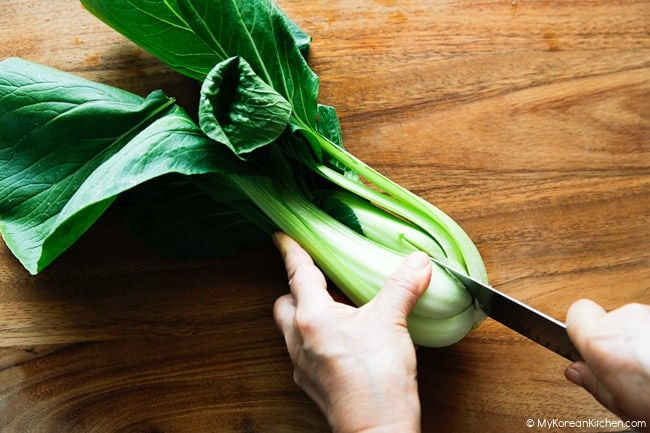 Slicing bok choy on a wooden cutting board for kimchi
