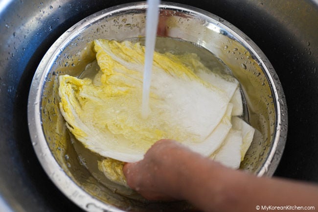 Salted napa cabbage leaves being rinsed under running water.