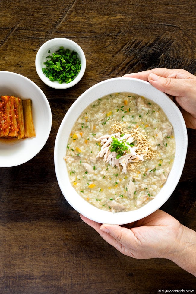 Holding a bowl of dakjuk, Korean chicken porridge, topped with shredded chicken and garnishes