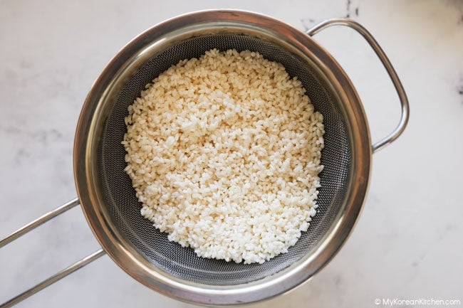 Rinsed and drained glutinous rice resting in a colander for Korean chicken porridge