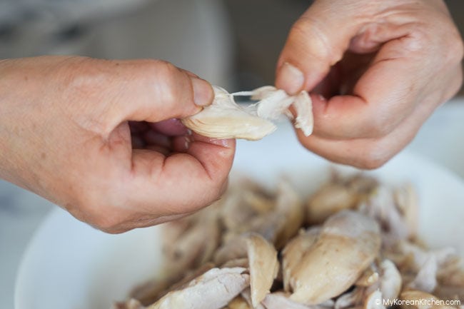 Cooked chicken being torn into pieces by hand