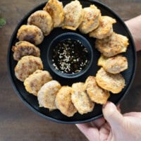 Korean meat patties on a black plate held in two hands.