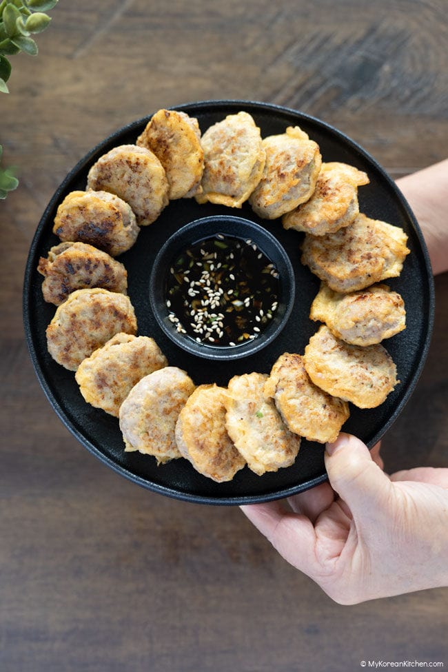 Korean meat patties on a black plate held in two hands.